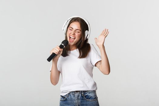 Carefree smiling girl playing karaoke, singing in microphone with headphones.
