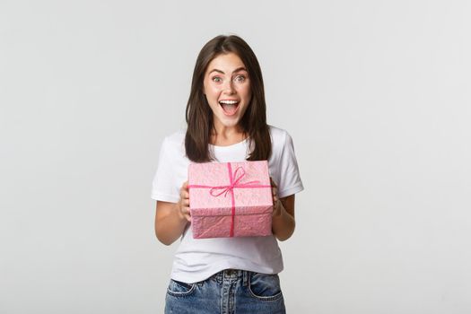 Surprised happy birthday girl receiving wrapped gift, white background.