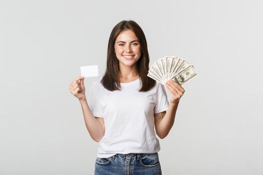 Portrait of excited smiling girl holding money and credit card, white background.