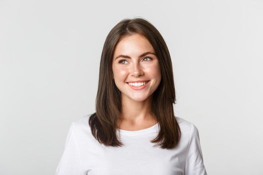 Portrait of attractive thoughtful girl smiling and looking left, white background.