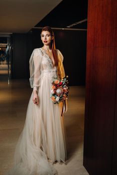 Stylish red-haired bride in a dress with sleeves and a bouquet in the interior.