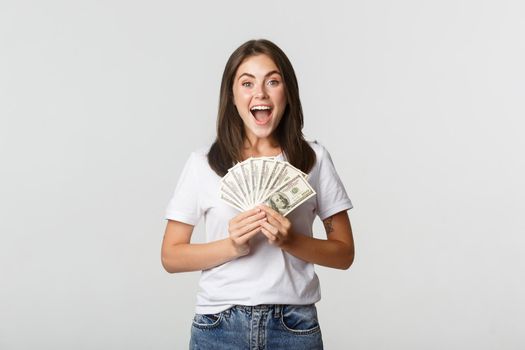 Happy attractive brunette girl holding money and smiling excited, white background.