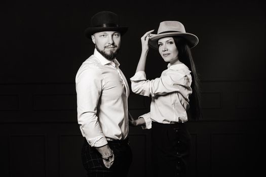 A man and a woman in white shirts and hats on a black background.A couple in love poses in the interior of the studio.black and white photo.