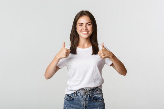 Happy satisfied young woman smiling, showing thumbs-up in approval, like something.