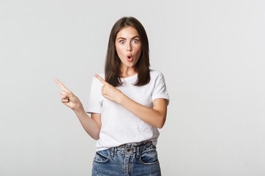 Excited beautiful girl smiling, pointing fingers upper left corner and looking amazed at logo.