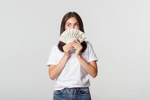 Excited dreamy girl holding money and looking upper left corner, thinking over white background.