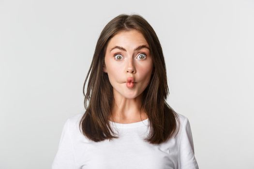 Close-up of funny and cute brunette girl suckink lips, making fish grimace, white background.
