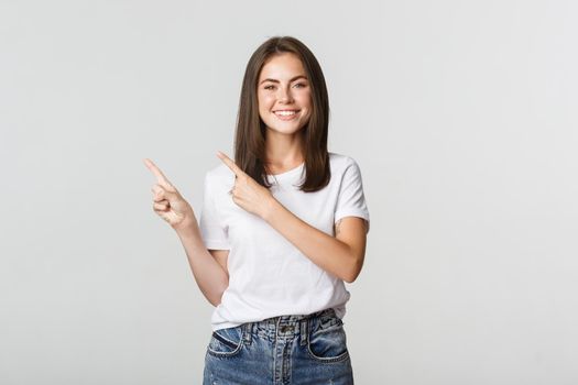 Satisfied smiling brunette girl pointing fingers upper left corner, showing logo.