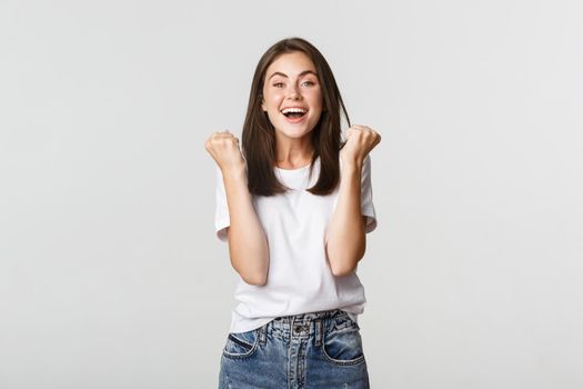 Cheerful attractive brunette girl fist pump and smiling with rejoice, winning.