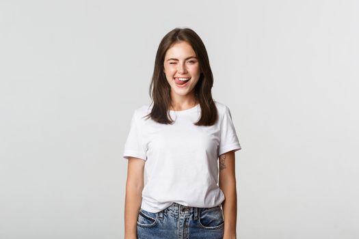 Sassy beautiful young woman winking and showing tongue flirty, white background.