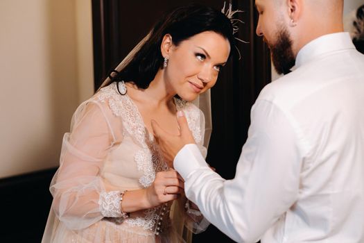 The bride in boudoir underwear dresses the groom in the interior of the hotel.