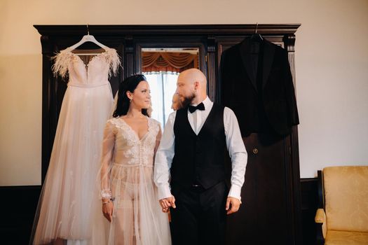 The bride in boudoir underwear dresses the groom in the interior of the hotel.