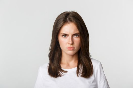 Close-up of pissed-off young girl frowning and looking angry at camera, white background.