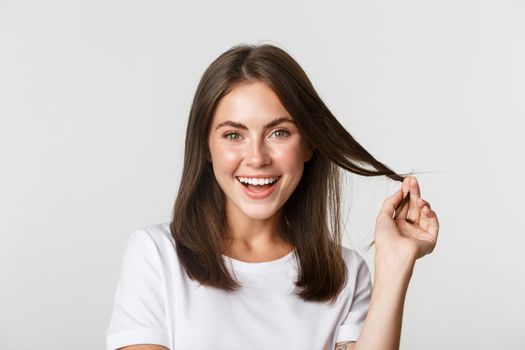 Portrait of flirty beautiful girl playing with hair and smiling at camera intrigued.