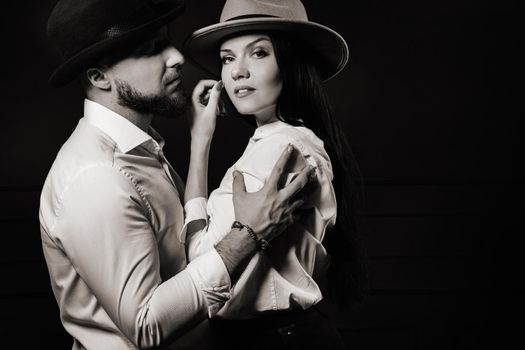 A man and a woman in white shirts and hats on a black background.A couple in love poses in the interior of the studio.black and white photo.