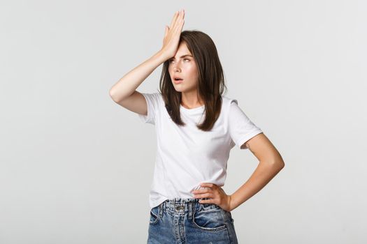 Bothered and annoyed young woman facepalm and roll eyes irritated.