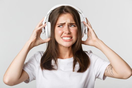 Close-up of annoyed beautiful girl in wireless headphones complaining awful music, grimacing bothered.