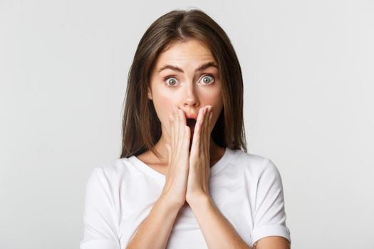 Close-up of shocked gasping brunette girl cover mouth with hands surprised.