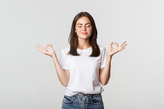 Relaxed smiling woman close eyes and meditating, do yoga, standing white background.
