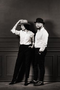 A man and a woman in white shirts and hats on a black background.A couple in love poses in the interior of the studio.black and white photo.