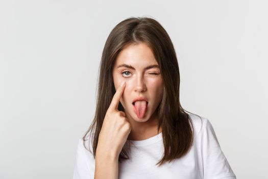 Close-up of silly attractive young girl showing tongue and pulling eyelid, watching you.