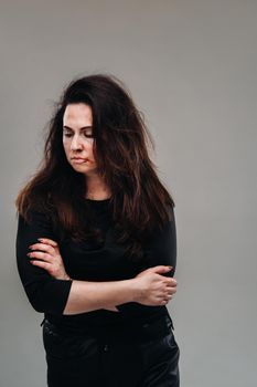 a battered woman in black clothes on an isolated gray background. Violence against women.