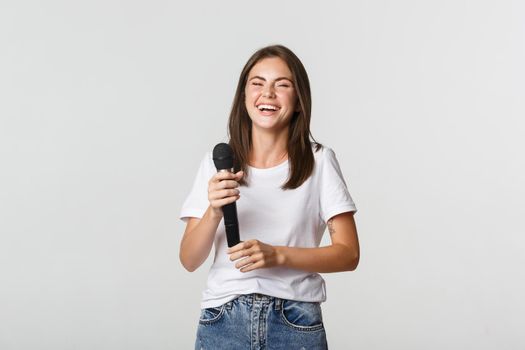 Happy laughing girl holding microphone and singing karaoke, white background.