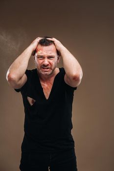 Against a gray background stands a battered angry man in a black T-shirt with wounds.