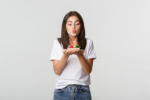 Excited and dreamy cute birthday girl making wish on b-day cake, blowing candle.