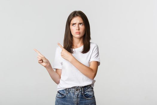 Upset cute girl pointing upper left corner, express regret.
