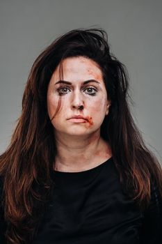 a battered woman in black clothes on an isolated gray background. Violence against women.