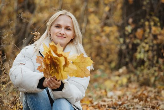 Portrait of a young blonde woman in the autumn forest, with a bouquet of yellow leaves in her hands.
