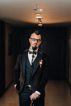 The groom in a tuxedo and bow tie with a mohawk hairstyle and a cane in the interior.