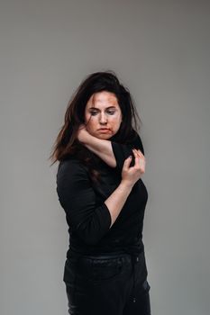 a battered woman in black clothes on an isolated gray background. Violence against women.