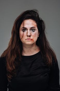 a battered woman in black clothes on an isolated gray background. Violence against women.