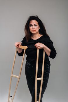 A battered woman in black clothes with casters in her hands on a gray background.