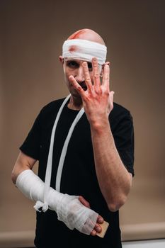 A battered man with a bandaged head and a cast on his arm stands on a gray background.