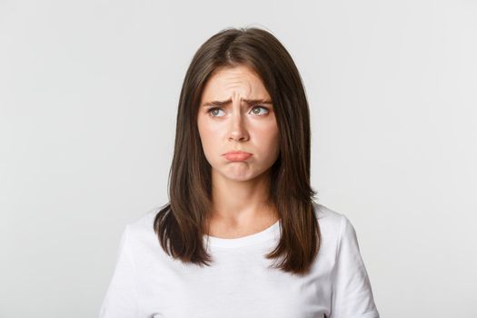 Close-up of sulking upset cute girl looking upper left corner with jealousy, standing sad over white background.