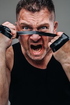 on a gray background stands a battered man in a black T shirt looking like a fighter and preparing for a fight.