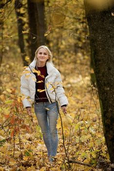 Portrait of a young blonde woman in the autumn forest, with a bouquet of yellow leaves in her hands.