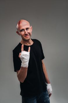 On a gray background stands a battered man in a black T-shirt With his hands wrapped up.