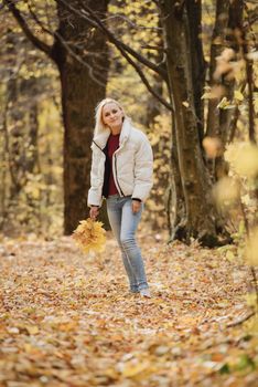 Portrait of a young blonde woman in the autumn forest, with a bouquet of yellow leaves in her hands.