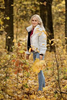 Young blonde woman in the autumn forest, with a bouquet of yellow leaves in her hands.