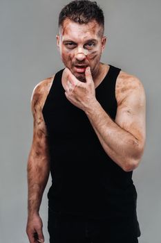 a battered man in a black T shirt who looks like a drug addict and a drunk stands against a gray background.