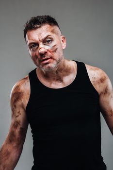 a battered man in a black T shirt who looks like a drug addict and a drunk stands against a gray background.