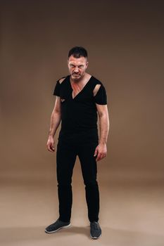 Against a gray background stands a battered angry man in a black T-shirt with wounds.