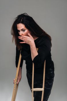 A woman beaten in black clothes with crutches in her hands on a gray background.