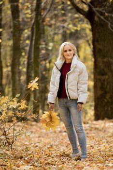 Portrait of a young blonde woman in the autumn forest, with a bouquet of yellow leaves in her hands.