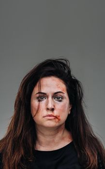 a battered woman in black clothes on an isolated gray background. Violence against women.