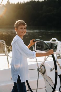 a little captain at the helm on a yacht. a little boy at the helm of the captain on a yacht at sunset.